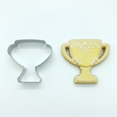 Trophy-shaped cookie cutter next to a yellow trophy cookie